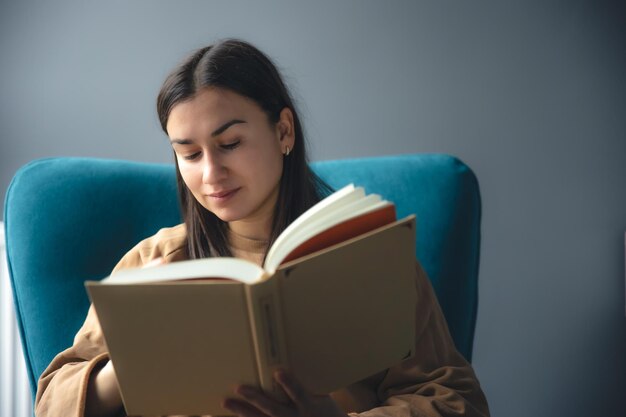 Foto grátis uma jovem está lendo um livro enquanto está sentada em uma cadeira