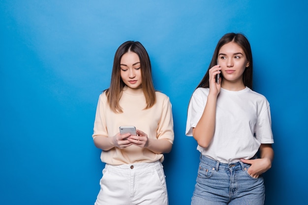 Uma jovem falando ao telefone e outra garota usando o telefone em uma parede azul