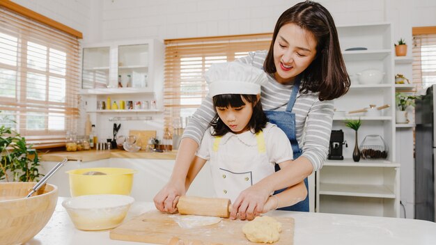 Uma jovem família asiática japonesa e feliz e sorridente com crianças em idade pré-escolar se divertem cozinhando bolos