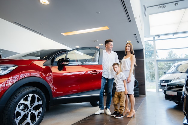Uma jovem família feliz escolhe e compra um carro novo em uma concessionária. comprando um carro novo.