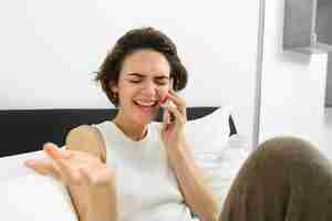 Foto grátis uma jovem feliz a ligar para uma amiga a conversar ao telefone deitada na cama e a ter uma conversa animada