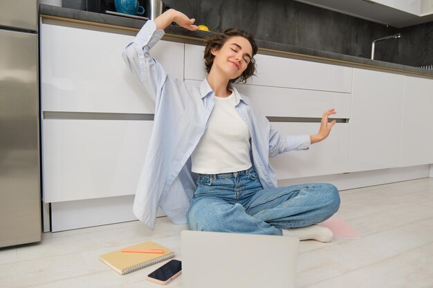 Foto grátis uma jovem feliz estica os braços, senta no chão com o laptop e termina seu trabalho remoto