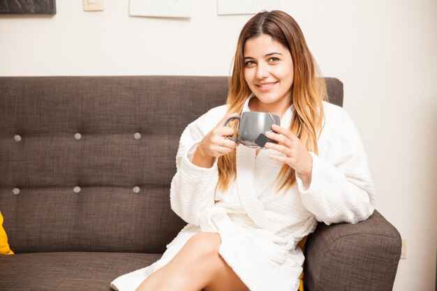 Uma jovem hispânica vestindo um roupão e esperando sua vez em um spa enquanto relaxa e bebe chá