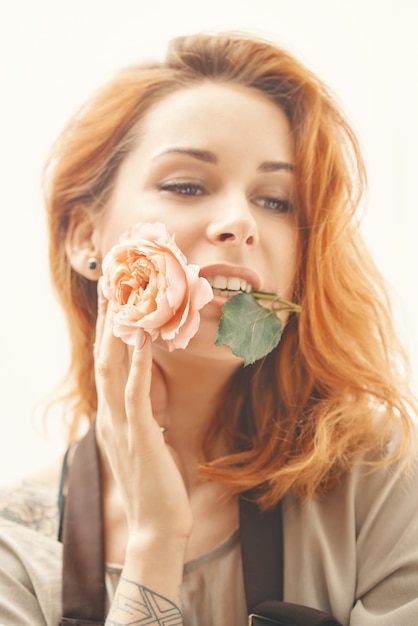 Uma jovem linda com cabelo vermelho está segurando uma rosa na boca