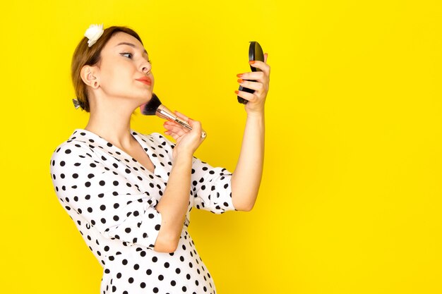 Uma jovem linda mulher de frente para um vestido de bolinhas preto e branco fazendo maquiagem em amarelo