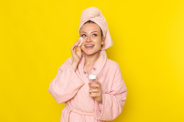 Uma jovem linda mulher de roupão rosa limpando a maquiagem com limpador