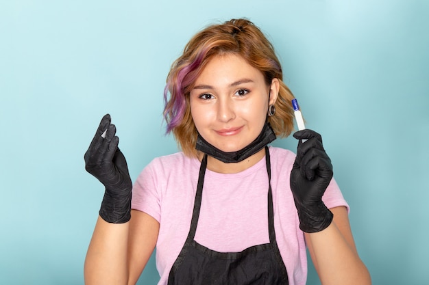 Uma jovem manicure feminina, vista de frente, com uma camiseta rosa e uma capa preta com luvas pretas sorrindo em azul