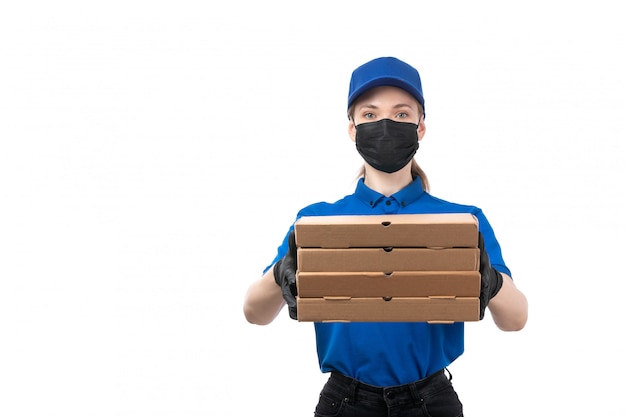 Uma jovem mensageira de frente com luvas pretas de uniforme azul e máscara preta segurando pacotes de entrega de comida