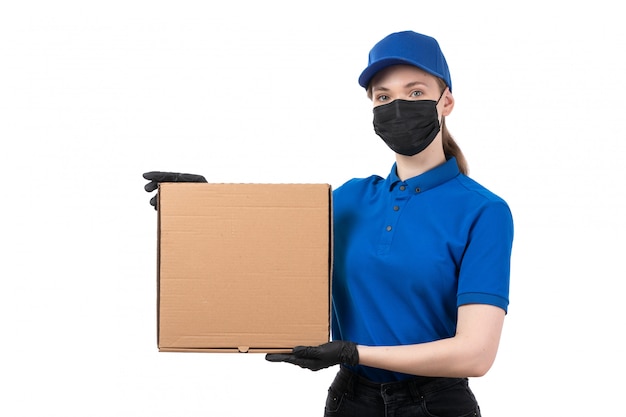 Uma jovem mensageira de frente com luvas pretas de uniforme azul e máscara preta segurando um pacote de comida