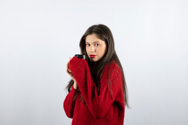 Uma jovem modelo com um suéter vermelho segurando uma xícara de café