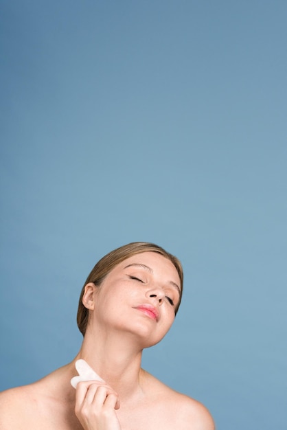 Uma jovem mulher caucasiana está fazendo massagem no pescoço usando um tiro gua sha vertical