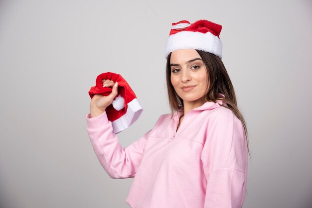 Uma jovem mulher com chapéu de Papai Noel vermelho segurando um chapéu.