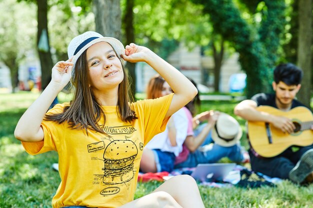 Uma jovem mulher com seus amigos se divertindo no parque, sentada na grama