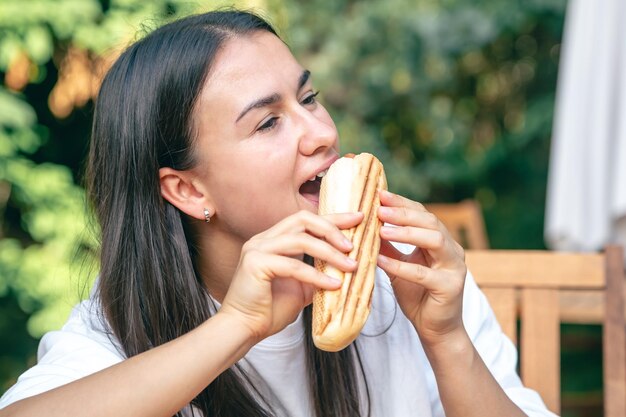 Uma jovem mulher come um cachorro-quente em um terraço de café