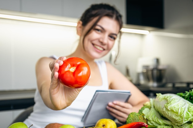 Uma jovem na cozinha com um bloco de notas e um tomate na mão