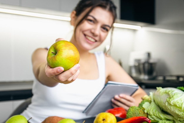 Foto grátis uma jovem na cozinha com um bloco de notas e uma maçã na mão