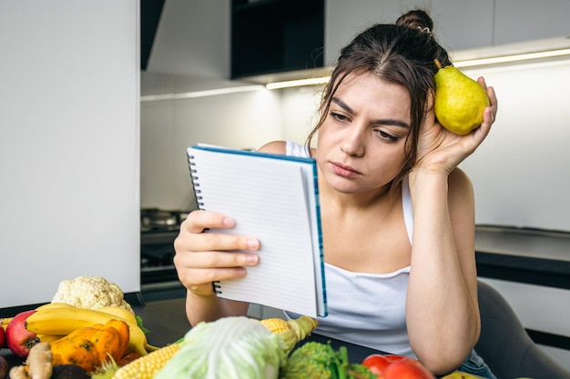 Foto grátis uma jovem na cozinha com um notebook entre legumes