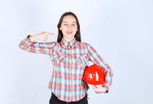 Uma jovem segurando um capacete vermelho e apontando para o lado com o dedo.