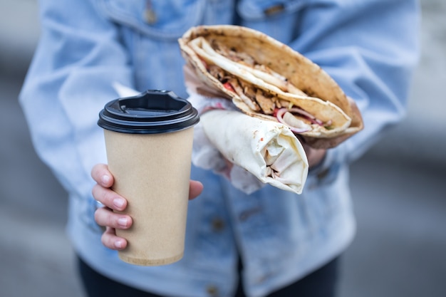 Uma jovem segurando um copo de café e fast food.