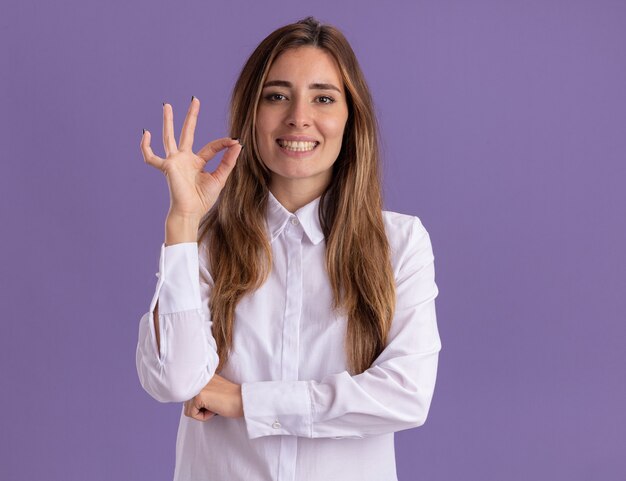 Uma jovem sorridente e bonita caucasiana gesticulando com a mão ok sinal isolada na parede roxa com espaço de cópia