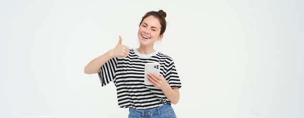 Foto grátis uma jovem sorridente mostrando o polegar para cima em aprovação recomenda que o aplicativo mantenha o smartphone parece satisfeito