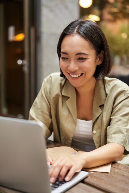 Uma jovem sorridente trabalhando em um café ou espaço de coworking sentada com um laptop estudando ou fazendo homew