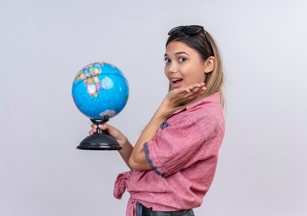 Uma jovem surpresa, vestindo uma camisa vermelha, segurando um globo enquanto olha