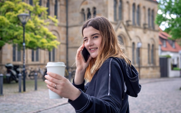 Uma jovem tomando café e falando ao telefone em uma caminhada na cidade