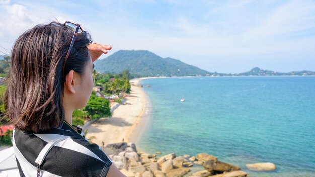 Uma jovem turista está olhando para o mar e a bela paisagem natural no mirante da praia de lamai durante a viagem de verão na ilha de koh samui, surat thani, tailândia, tela panorâmica 16: 9