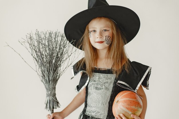 Uma jovem vestida de preto como uma bruxa tem um chapéu em forma de cone na cabeça. Menina segurando uma vassoura e uma abóbora