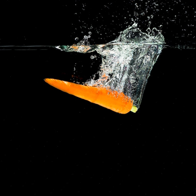 Uma laranja cenoura caindo em respingos de água contra um fundo preto