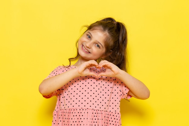 Foto grátis uma linda criança com um vestido rosa sorrindo e mostrando sinal de amor