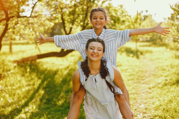 Foto grátis uma linda e uma linda mãe de cabelos compridos em um vestido azul de pé em um parque solar e jogando