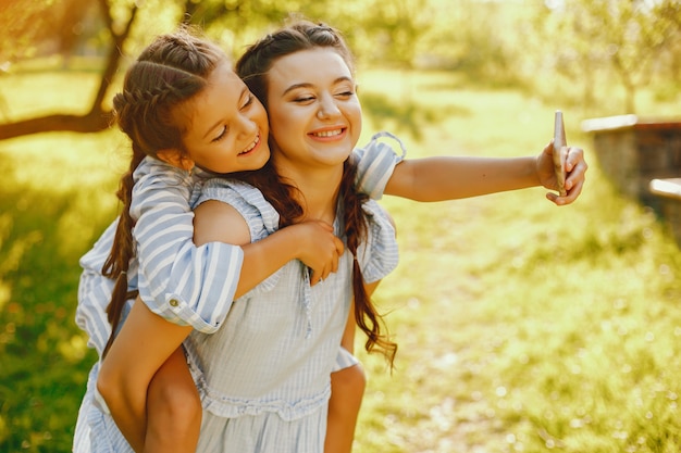 Foto grátis uma linda e uma linda mãe de cabelos compridos em um vestido azul de pé em um parque solar e jogando