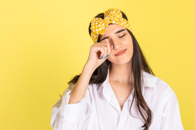 Foto grátis uma linda garota de pé sobre um fundo amarelo e coçando os olhos