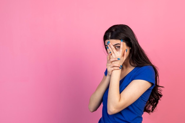 Uma linda garota fecha os olhos com a mão I39m olhando por entre os dedos Foto de alta qualidade