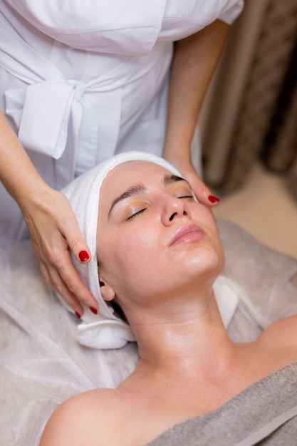 Uma linda jovem deita-se na mesa da esteticista e recebe procedimentos, uma leve massagem facial.