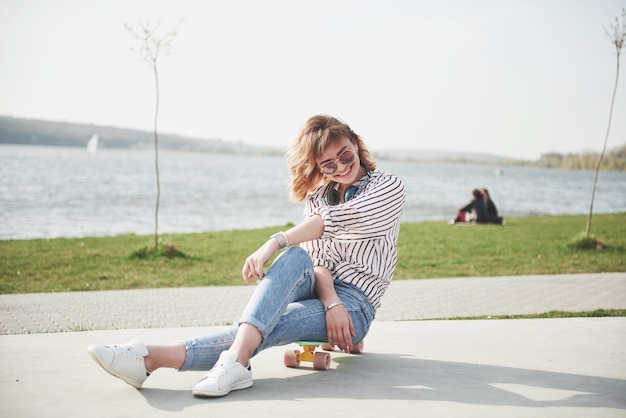 Uma linda jovem está se divertindo no parque e andando de skate.