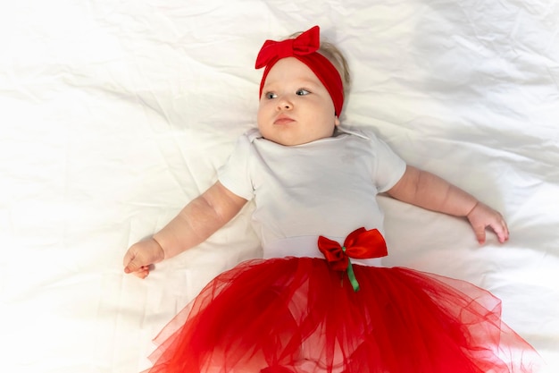 Uma linda menina recém-nascida está deitada em um cobertor branco vestida com uma saia vermelha e com um laço vermelho em um