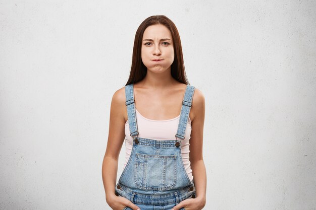 Uma linda mulher de aparência européia vestida de macacão jeans, prendendo a respiração, tentando não rir.