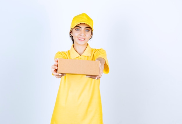 Uma linda mulher de uniforme amarelo segurando uma caixa de papel artesanal em branco.