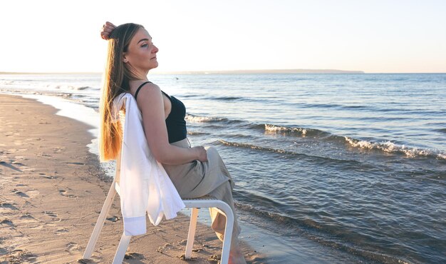 Uma linda mulher se senta em uma cadeira perto do mar