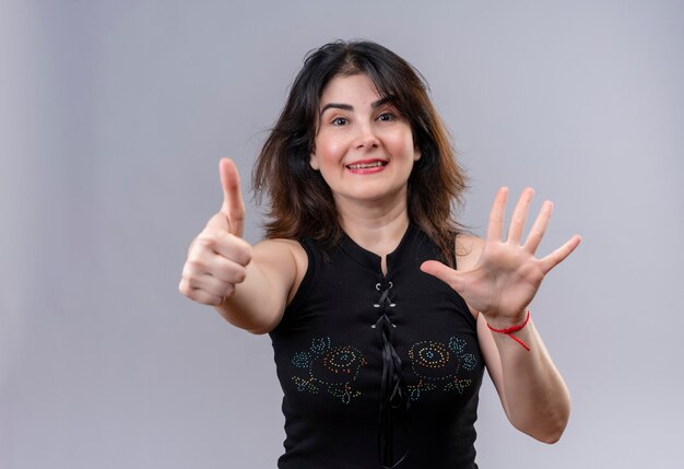Uma linda mulher usando blusa preta, fazendo um feliz polegar para cima e mostrando cinco sinais