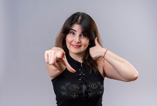 Uma linda mulher usando blusa preta sorrindo, mostrando seu sinal legal fazendo um feliz sinal de positivo