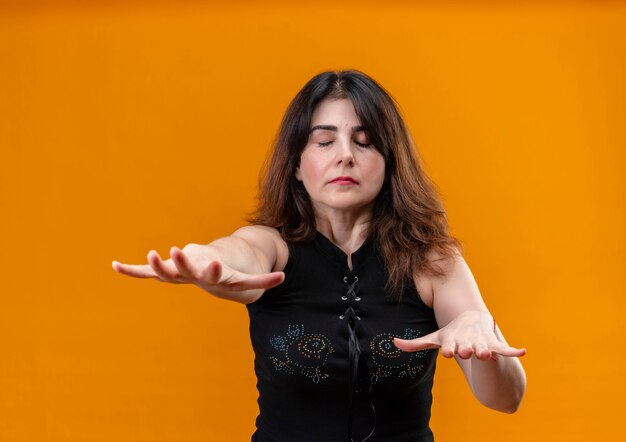 Uma linda mulher vestindo blusa preta e fechando os olhos sobre um fundo laranja