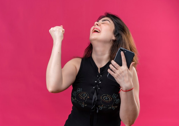 Uma linda mulher vestindo blusa preta se alegra com o telefone na mão