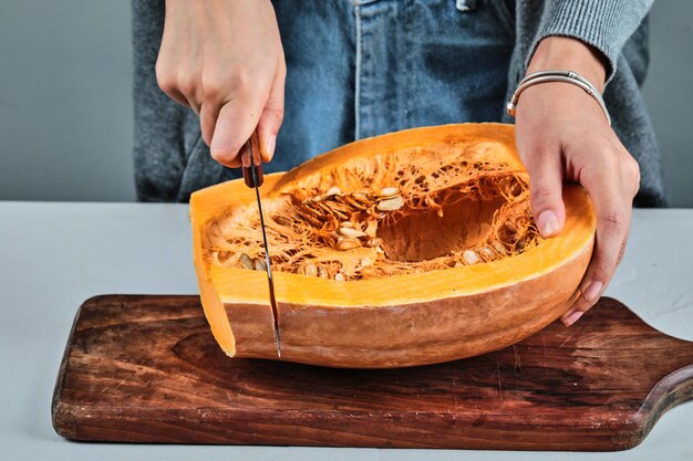 Uma mão de mulher cortando uma fatia de Pumpkon com uma faca na placa de madeira.
