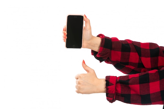 Uma mão feminina vista frontal na camisa quadriculada preto-vermelho segurando o smartphone em branco