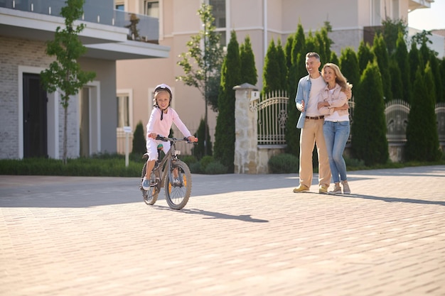 Uma menina andando de bicicleta enquanto seus pais a observam