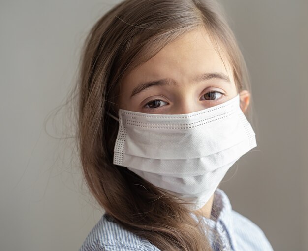 Uma menina bonitinha com uma máscara protetora descartável contra o coronavírus